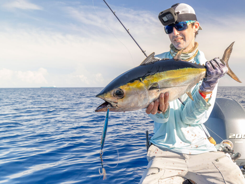 An angler holds a blackfin tuna with a jig hanging from its mouth.